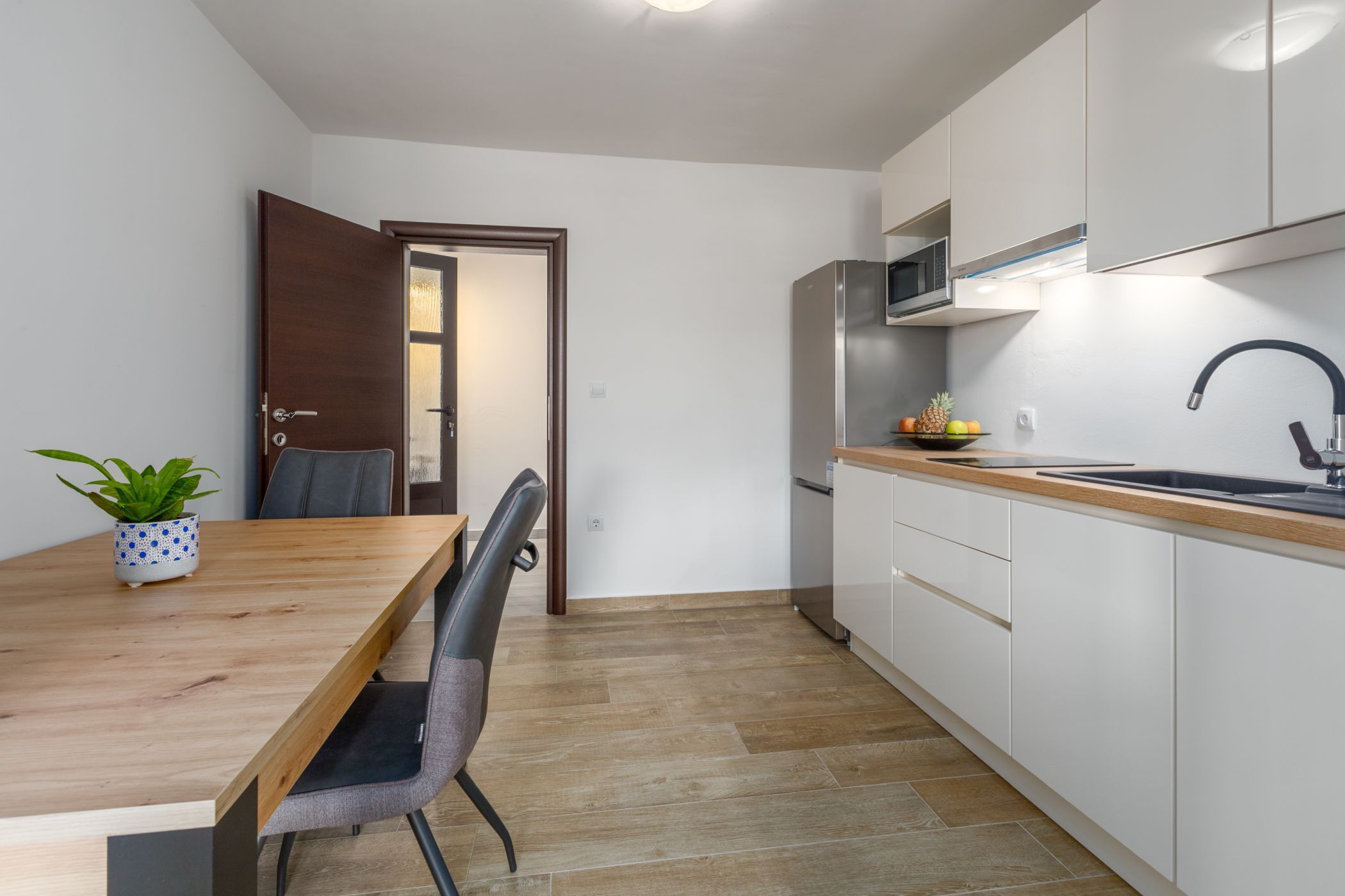 A compact kitchen with white cabinets, a wooden countertop, and a stainless steel refrigerator.