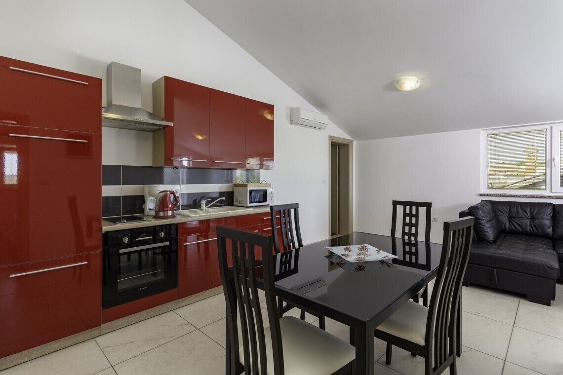 Una cocina compacta con armarios rojos, un comedor con mesa negra y un sofá negro.