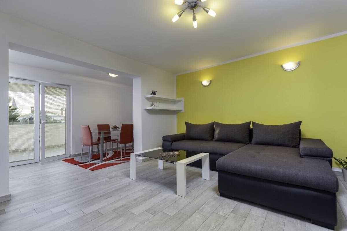 Una sala moderna con un sofá gris, una mesa de centro de vidrio y un comedor con sillas rojas.