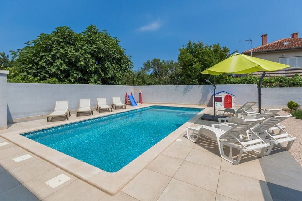 A rectangular swimming pool with clear blue water, surrounded by lounge chairs and a yellow umbrella.