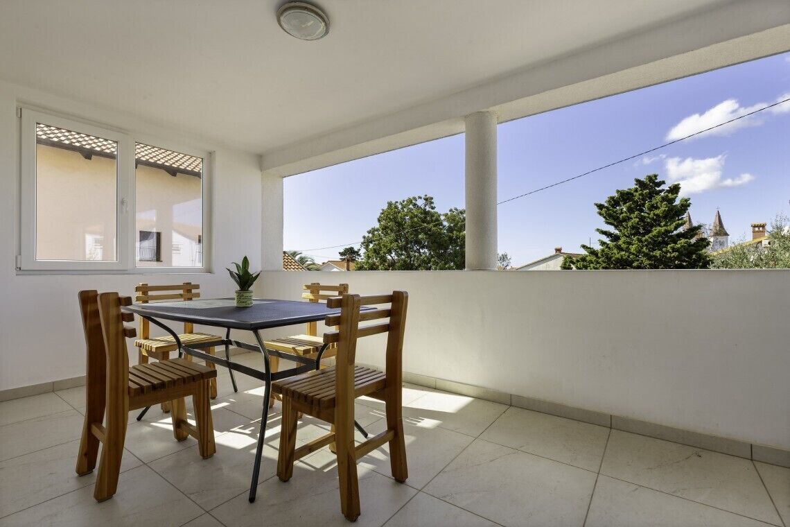 Ein Balkon mit Tisch, Stühlen, einer Topfpflanze und Blick auf Bäume und Gebäude.