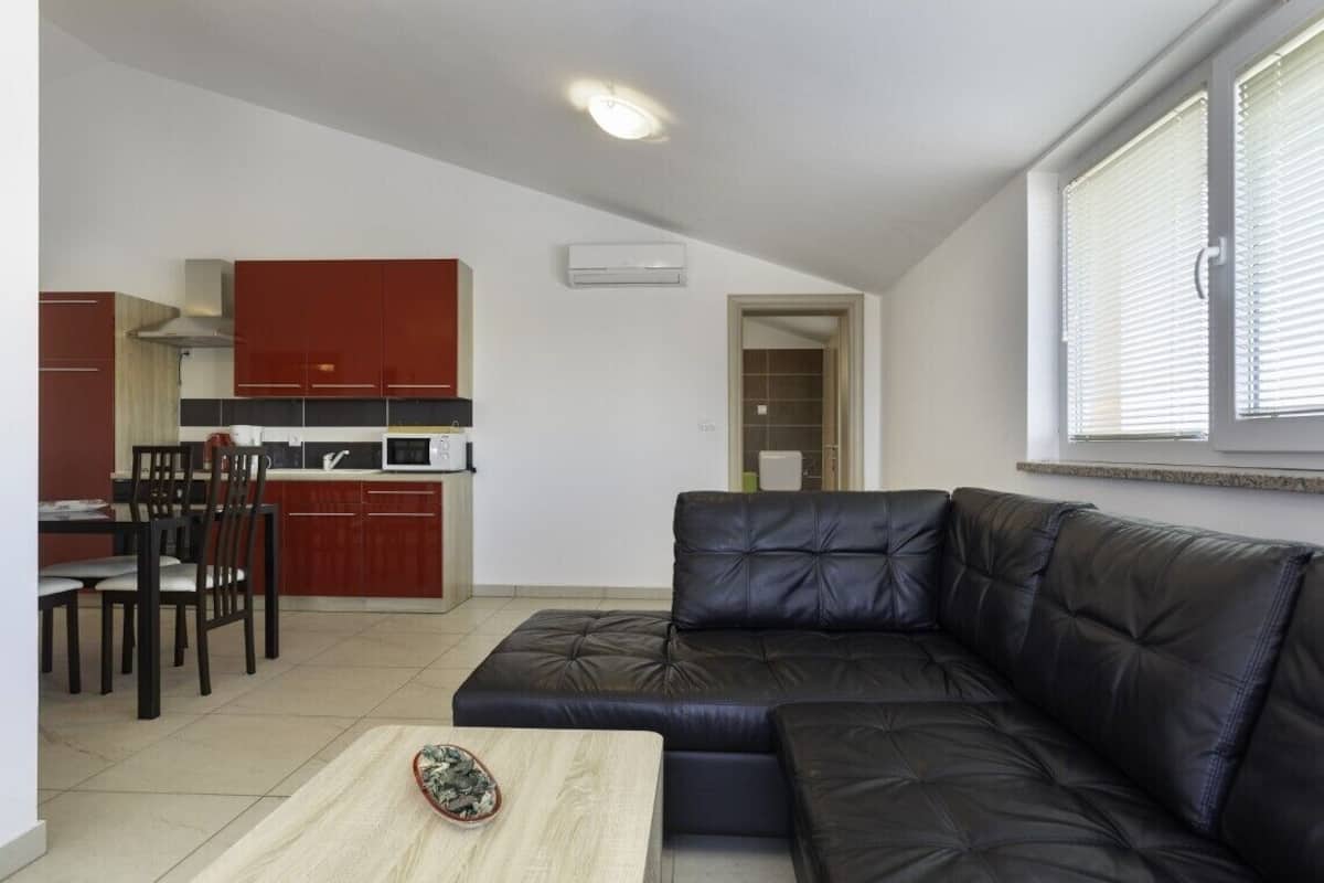 Una sala de estar moderna con un sofá de cuero negro, una mesa de comedor con sillas, y una cocina con armarios rojos y un microondas.