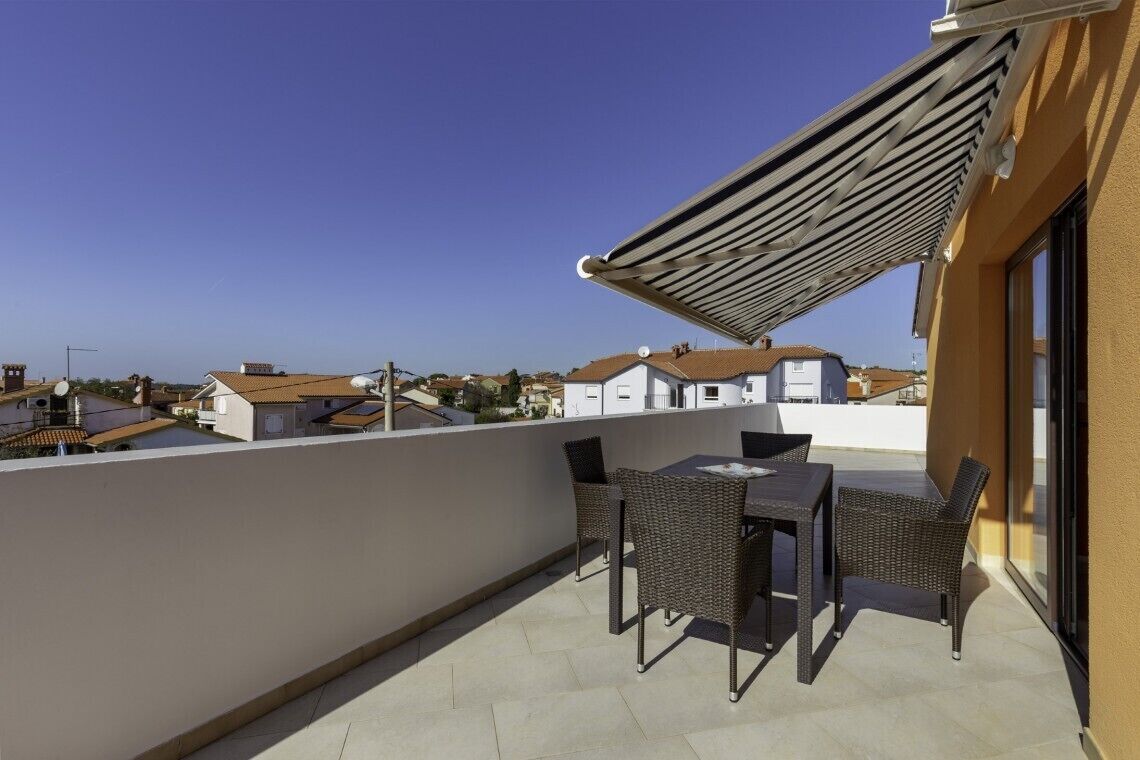 Un balcon avec une table et des chaises, un auvent rétractable et une vue sur les maisons voisines.
