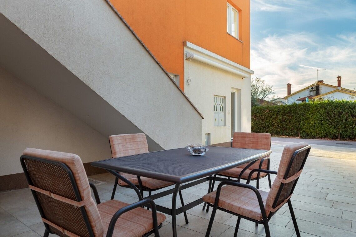 An outdoor patio with a table and chairs, a clear sky, and a building in the background.