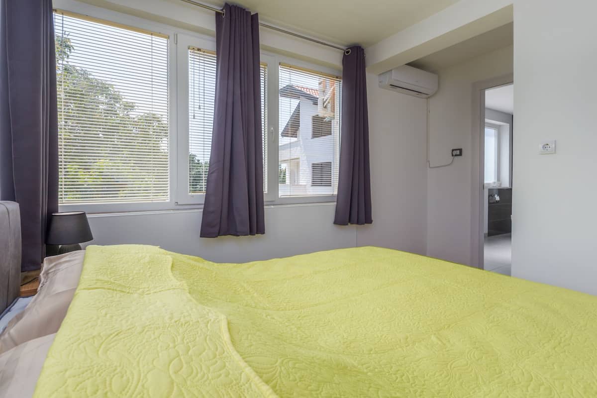 Un dormitorio con cama, ventana con cortinas y un equipo de aire acondicionado visible.