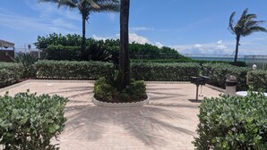 A paved courtyard with a central circular planter, surrounded by low hedges and palm trees. - Welcome to Paradise! (Jensen Beach)