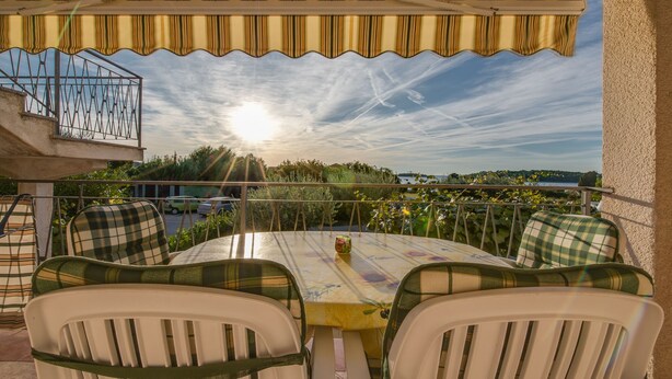 Eine Terrasse im Freien mit einem runden Tisch und Stühlen, Blick auf die Landschaft und einer Brüstung.