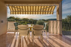A covered patio with two chairs and a table, a view of greenery and a body of water in the background. - Fiorela (Rovinj)