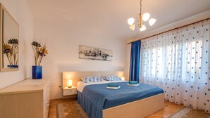 Ein Schlafzimmer mit einem hölzernen Bett, einem Nachttisch mit Lampe, einer blauen Vase mit Trockenblumen und einem Stadtbild an der Wand.