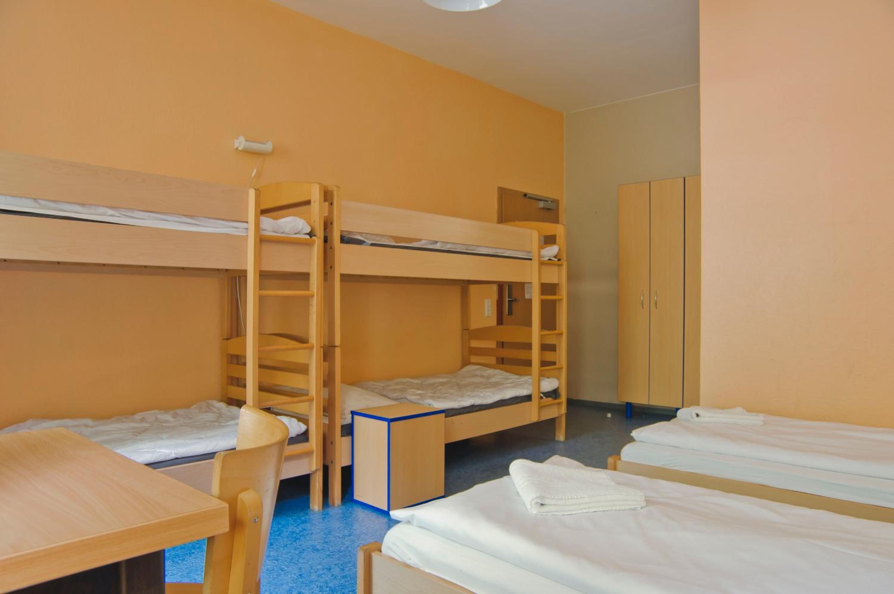 A dormitory room with bunk beds, a desk, and a wardrobe.