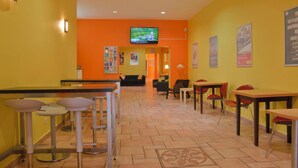 A brightly lit indoor space with yellow walls, a television mounted on the wall, and multiple seating areas including tables and chairs. - Happy Hotel Berlin (Berlin)