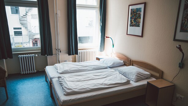 A hotel room with a bed, a bedside table, a lamp, and a window with curtains. - Happy Hotel Berlin (Berlin)