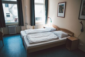 Una habitación de hotel con una cama, una mesita de noche, una lámpara y una ventana con cortinas.