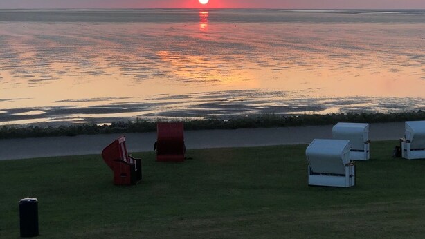 A sunset over a calm sea with lounge chairs on a grassy area. - Vacation home starboard quietly located large terrace only 300m to the beach / sea (Friedrichskoog-Spitze)
