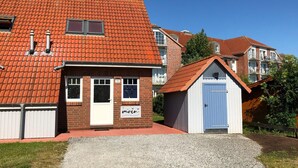 A residential building with a red-tiled roof, a small shed with a blue door, and a gravel driveway. - Vacation home starboard quietly located large terrace only 300m to the beach / sea (Friedrichskoog-Spitze)