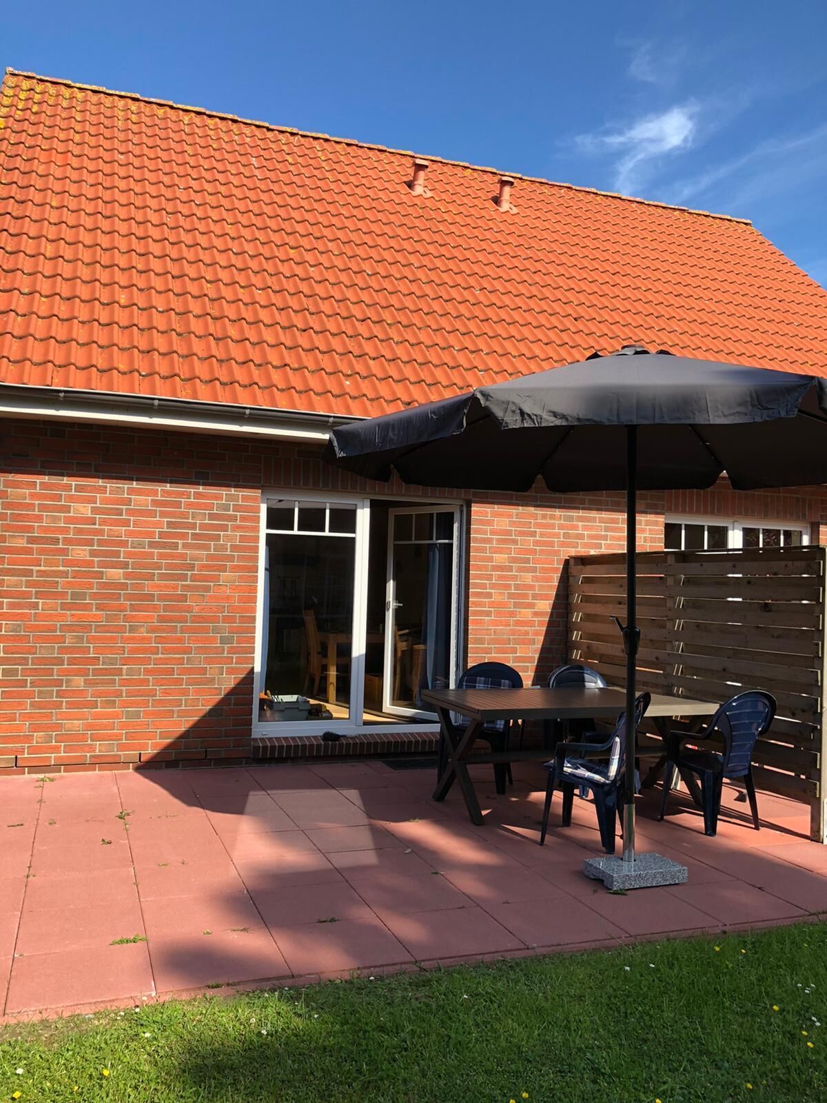 A patio with a brick house, a sliding glass door, and a table with chairs.