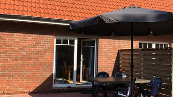 A patio with a brick house, a sliding glass door, and a table with chairs.