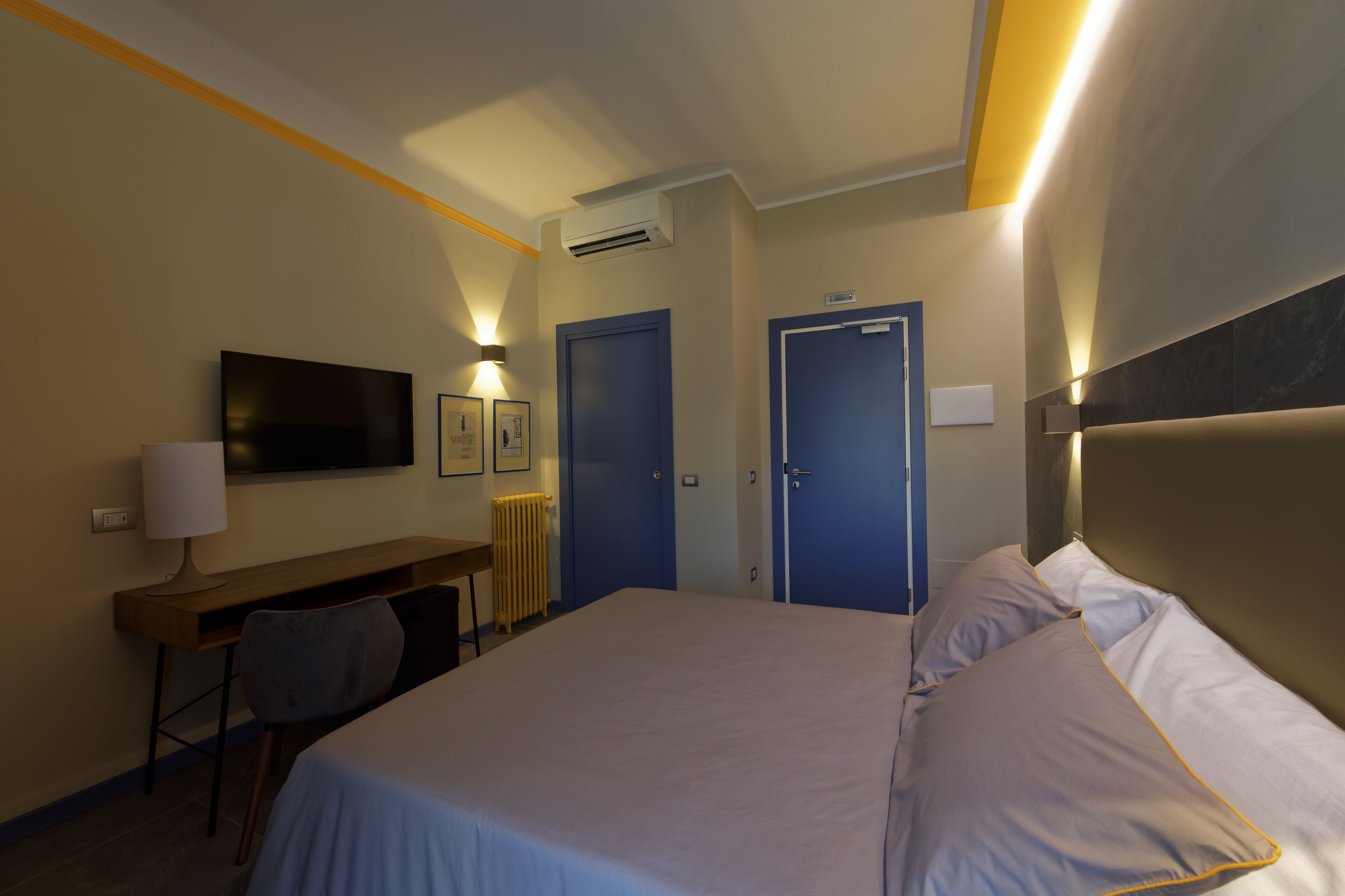 A hotel room with a bed, a desk, a chair, a TV, and two doors.