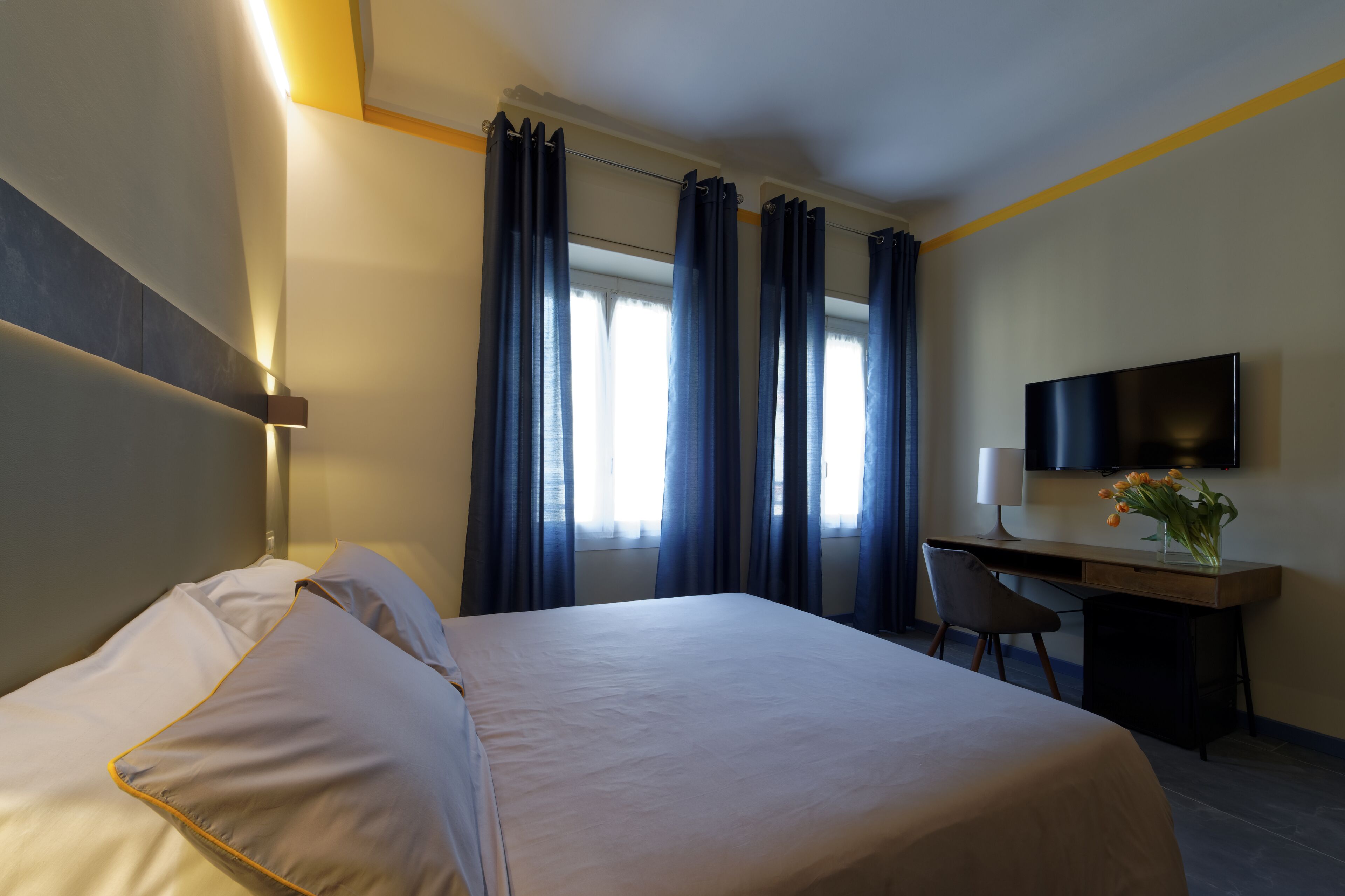 A hotel room with a bed, desk, chair, TV, and curtains.