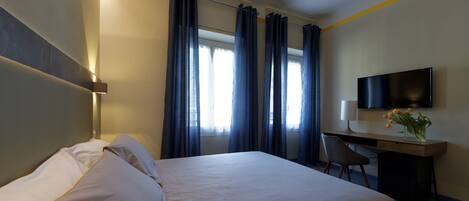 A hotel room with a bed, desk, chair, TV, and curtains.