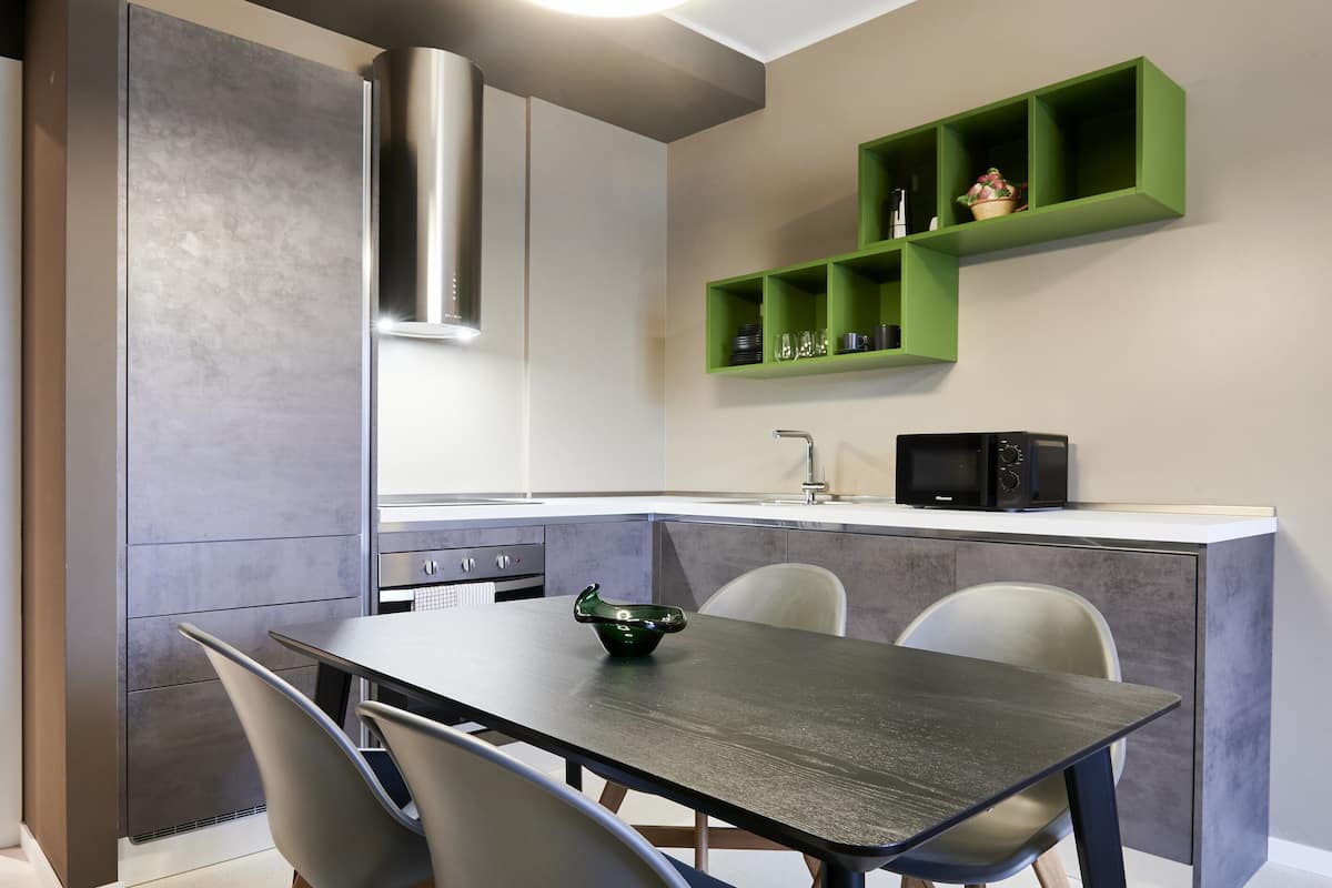 A modern kitchen with a built-in microwave, a stainless steel range hood, and a green shelf unit above the countertop.