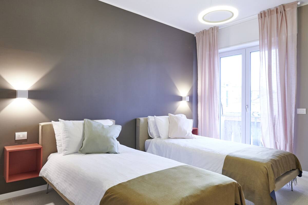 A hotel room with two beds, a nightstand, and a window with curtains.
