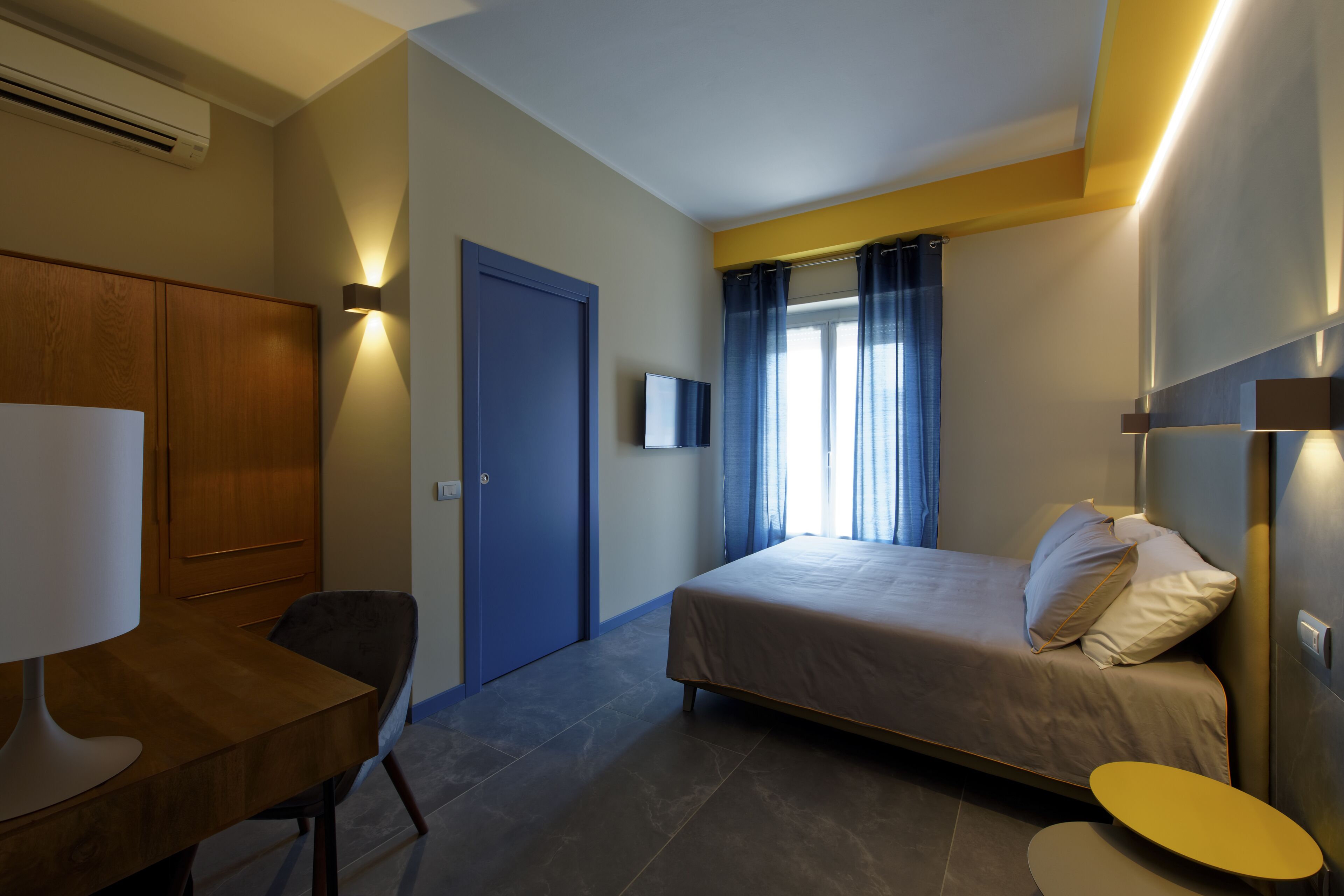 A bedroom with a bed, a desk, a chair, a wardrobe, and a TV.