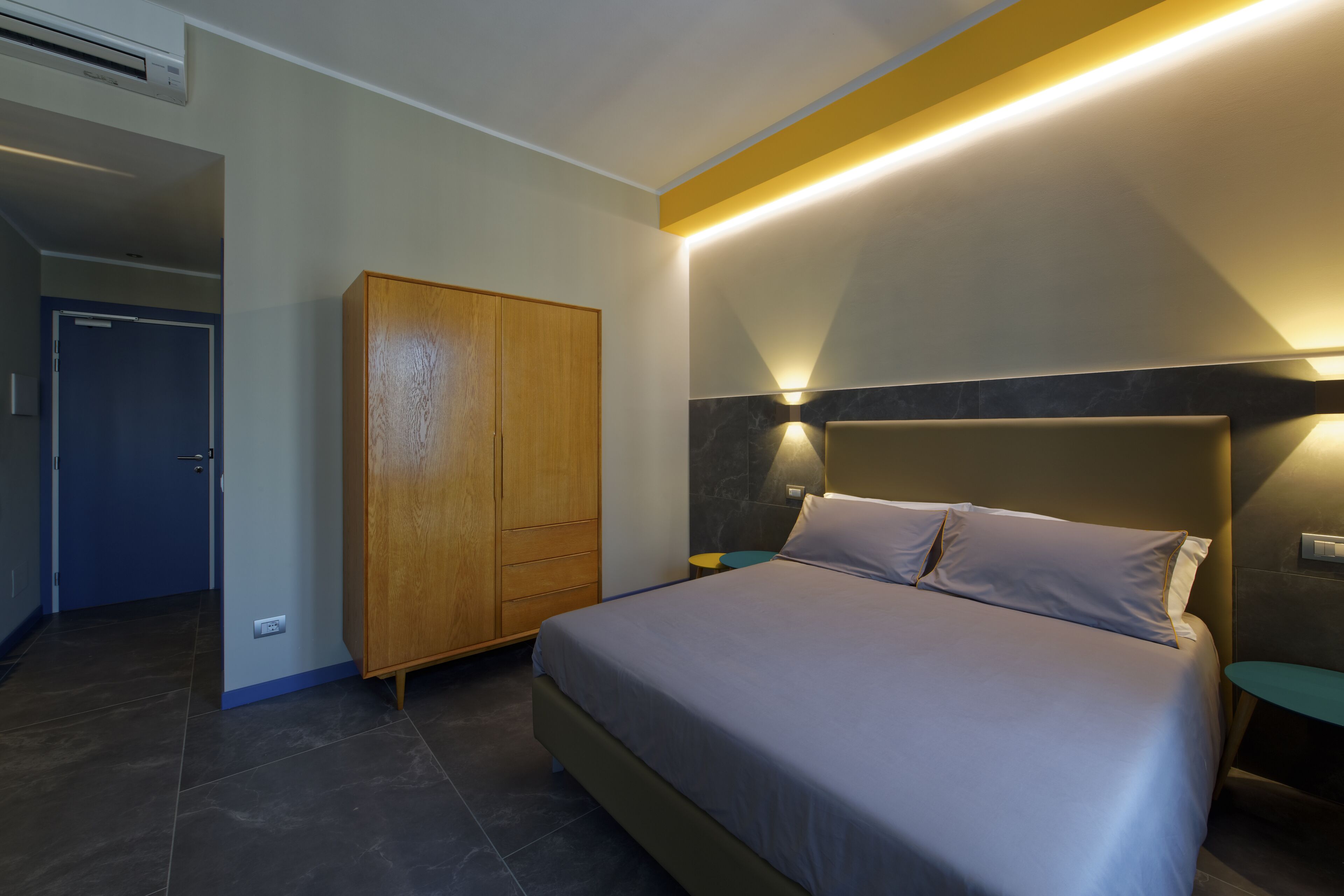 Een slaapkamer met een bed, een kledingkast, een nachtkastje en een wandlamp.