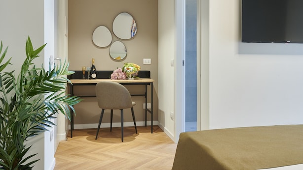 Quarto moderno com escrivaninha de madeira, uma cadeira, televisão na parede e um vaso com planta.