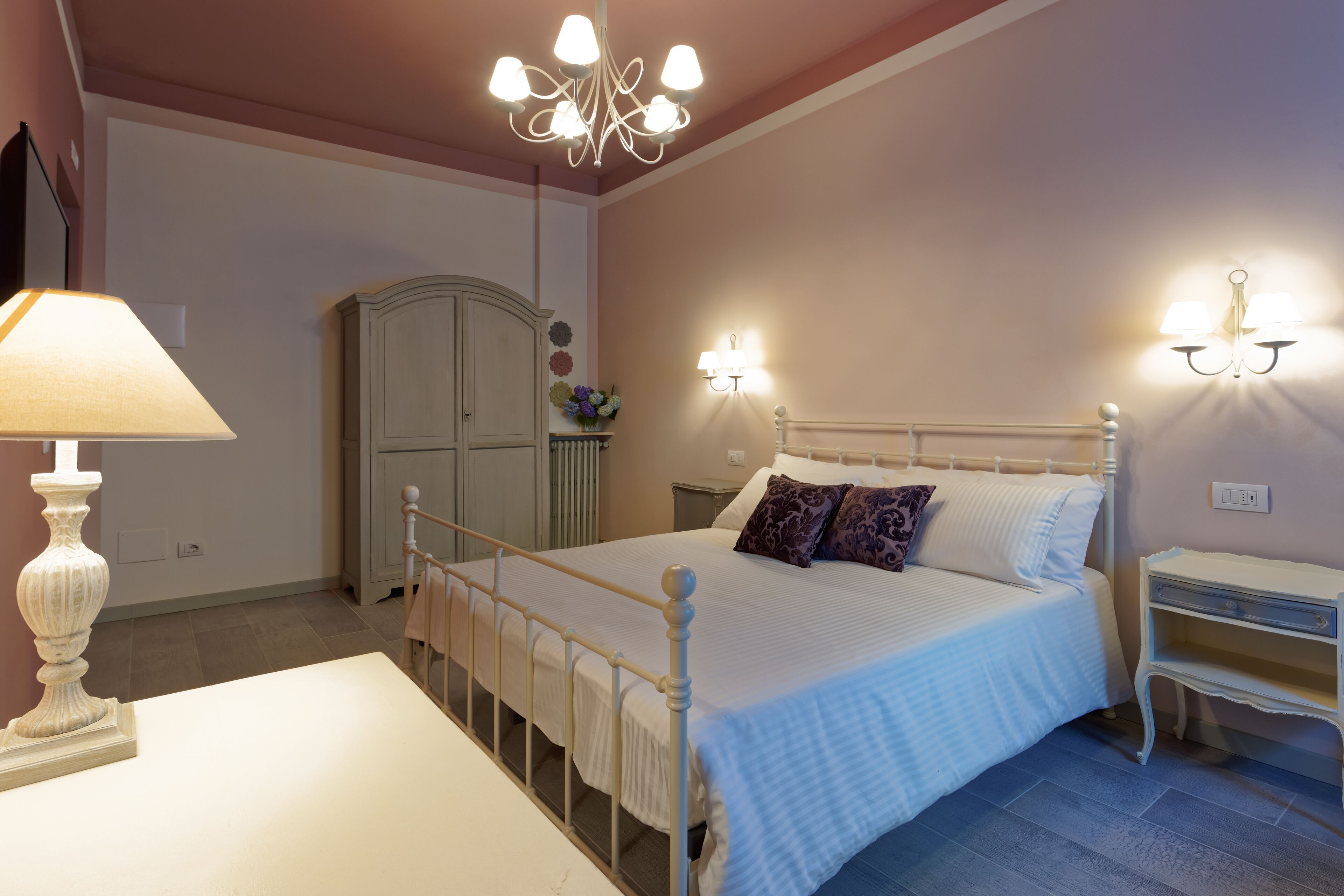 Un dormitorio con cama, mesitas de noche, lámpara, armario y apliques de pared.