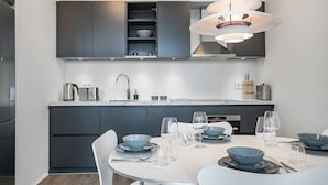 A modern kitchen with dark cabinetry, a white dining table set with blue bowls and wine glasses, and a pendant light above. - SIF Apartments Central Reykjavik - 1 Bedroom (Reykjavík)