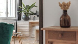 Una habitación con un escritorio de madera, una silla verde, una planta en maceta y un florero sobre un aparador.
