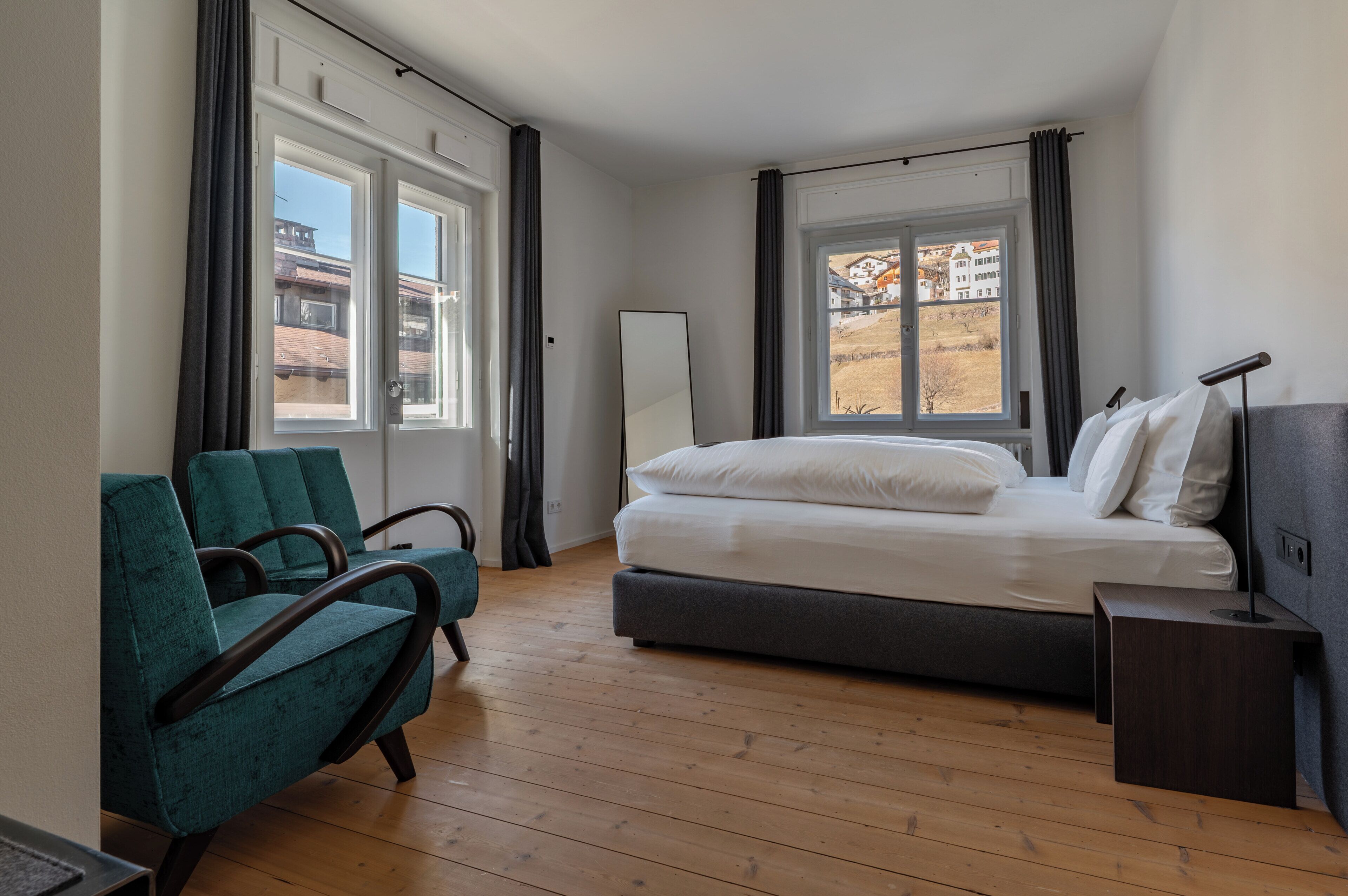 A bedroom with a bed, a chair, a bedside table, and a window with curtains.