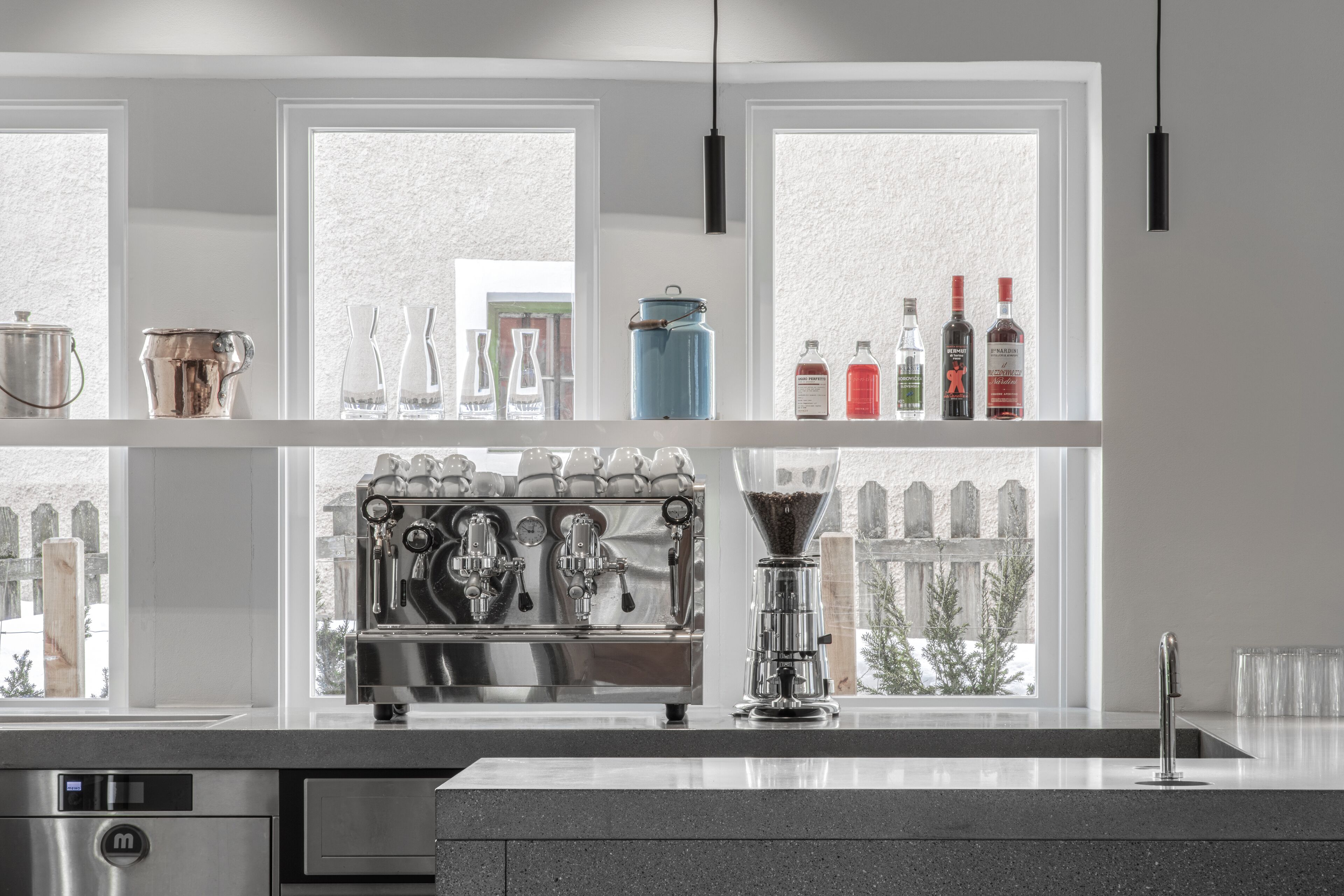 Een moderne keuken met een koffieapparaat, planken met flessen en uitzicht op een houten schutting.