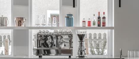 A modern kitchen with a coffee machine, shelves with bottles, and a view of a wooden fence.