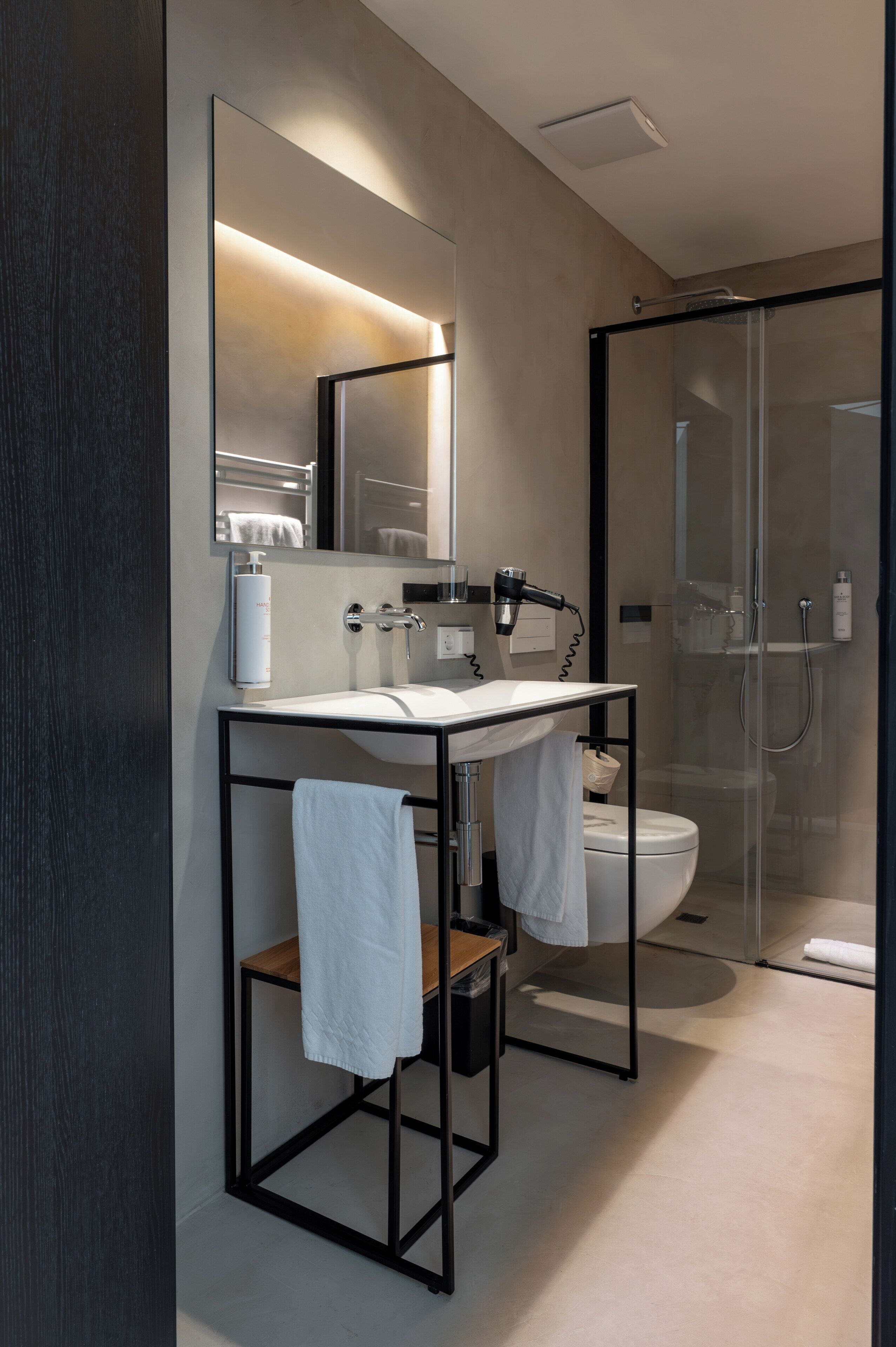 Un baño moderno con cabina de ducha de vidrio, lavamanos independiente y espejo sobre él.