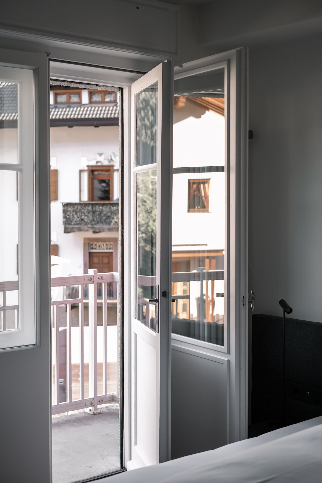 An open door leading to a balcony with a view of a building and a fence.