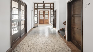 Un pasillo con piso moteado, puertas de madera y vistas a un balcón.