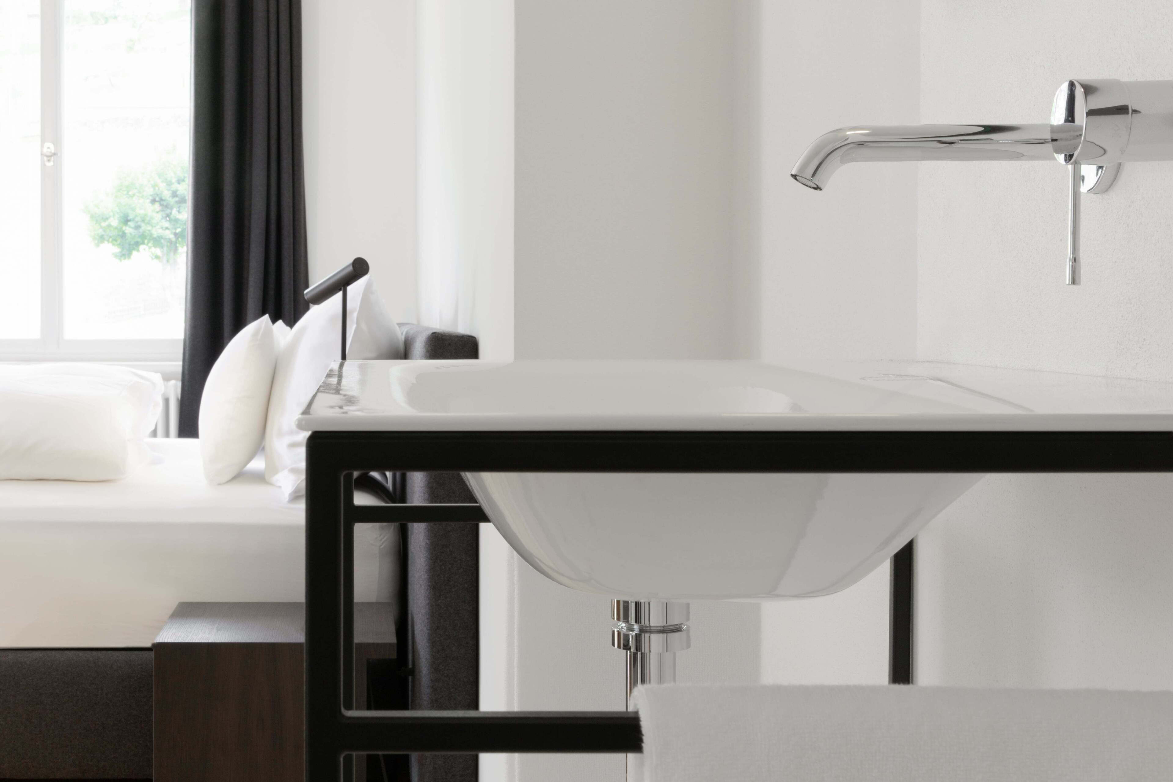 Un baño moderno con lavamanos blanco, grifo cromado y una ventana con cortinas negras.