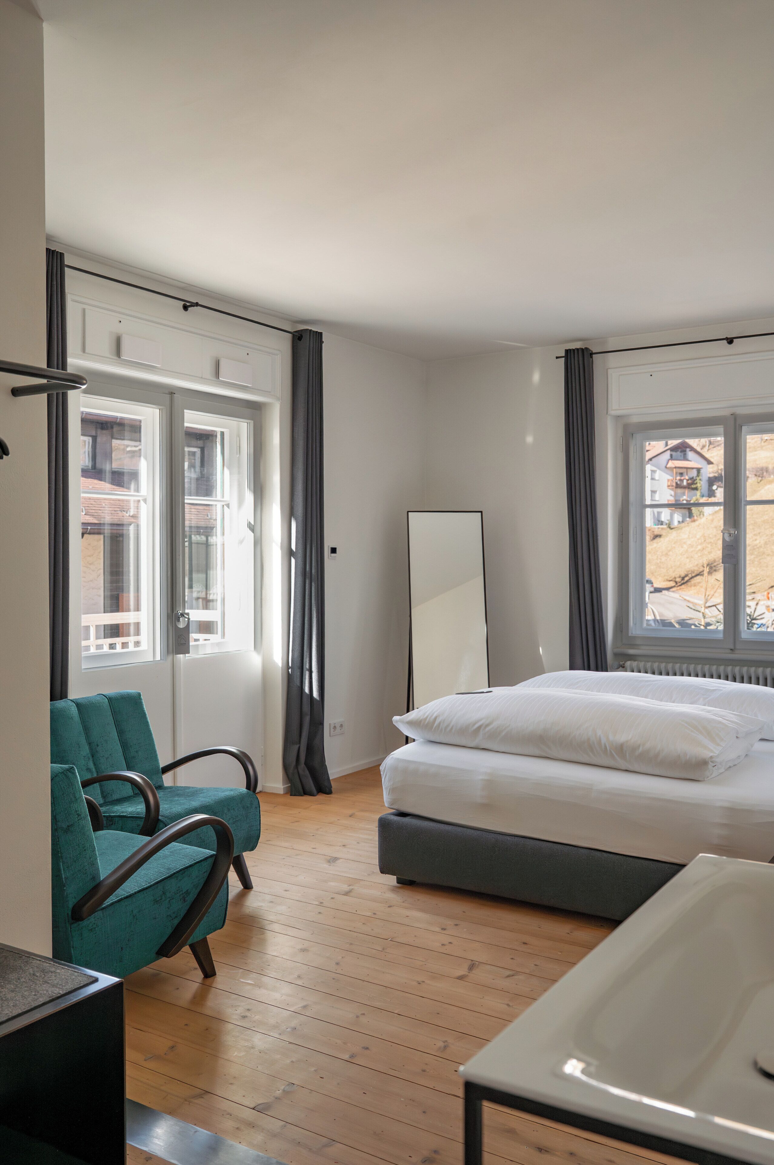 A bedroom with a bed, a chair, a mirror, and a window with curtains.