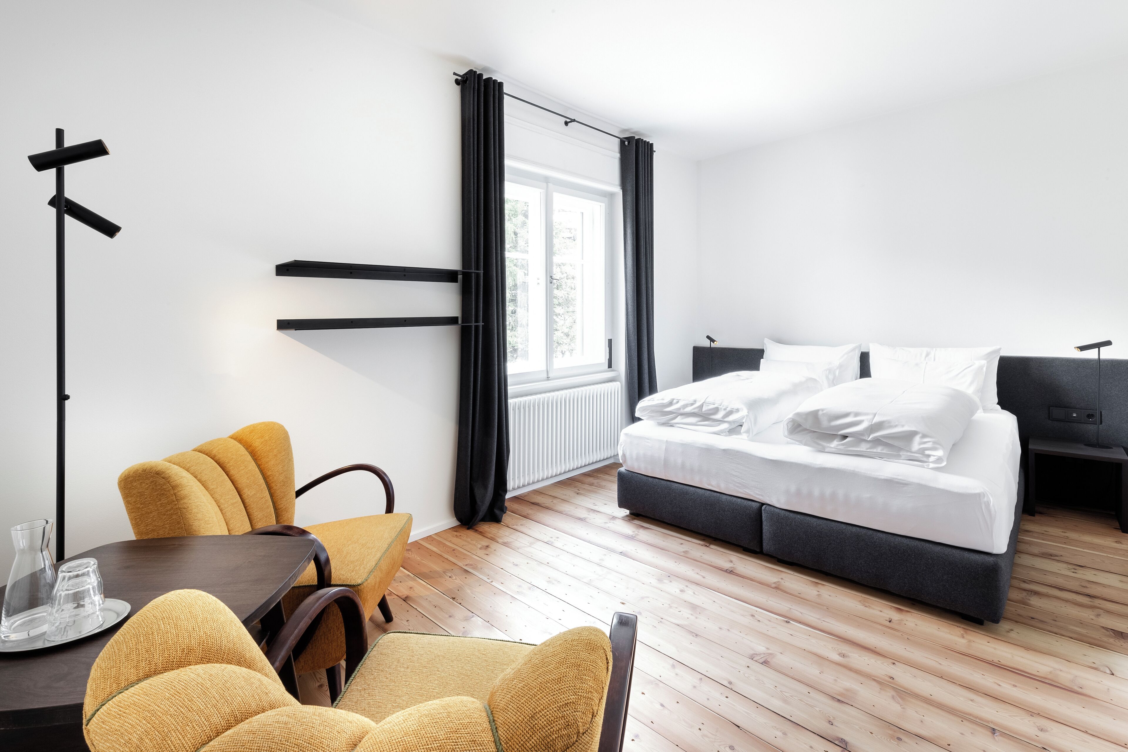 A modern bedroom with a bed, a desk with chairs, and a window with curtains.