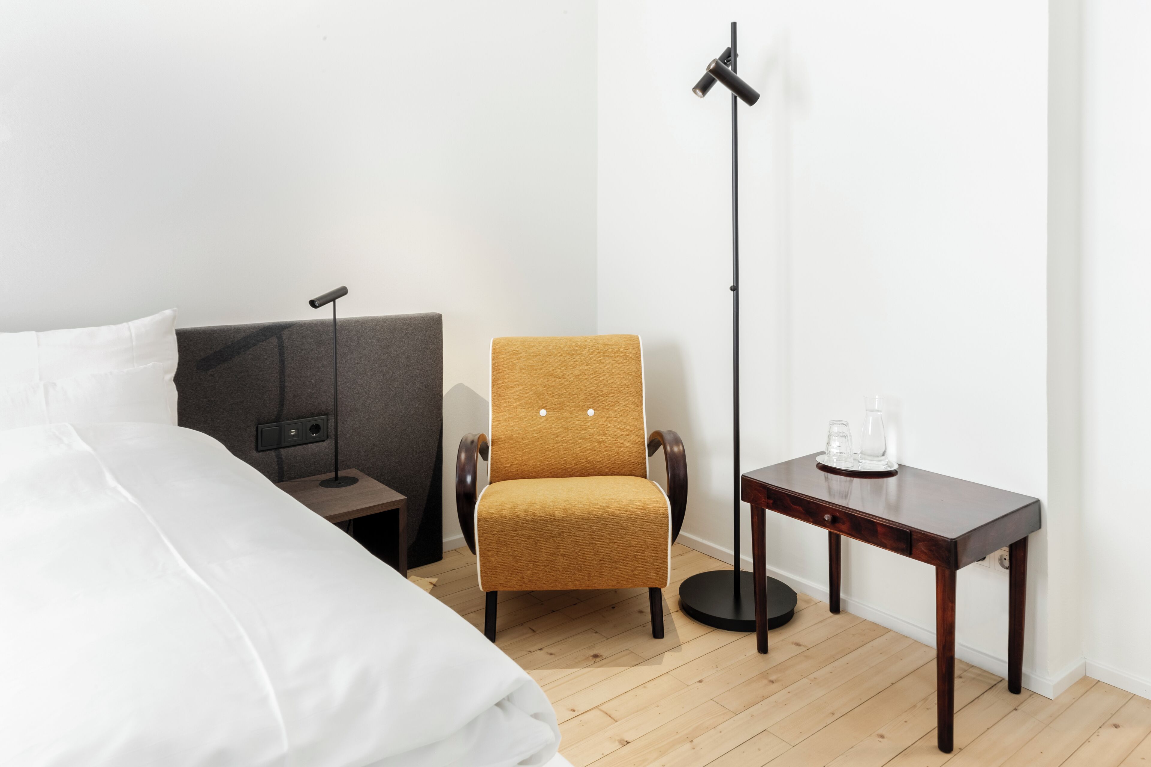 A hotel room with a bed, a chair, a desk, and a floor lamp.