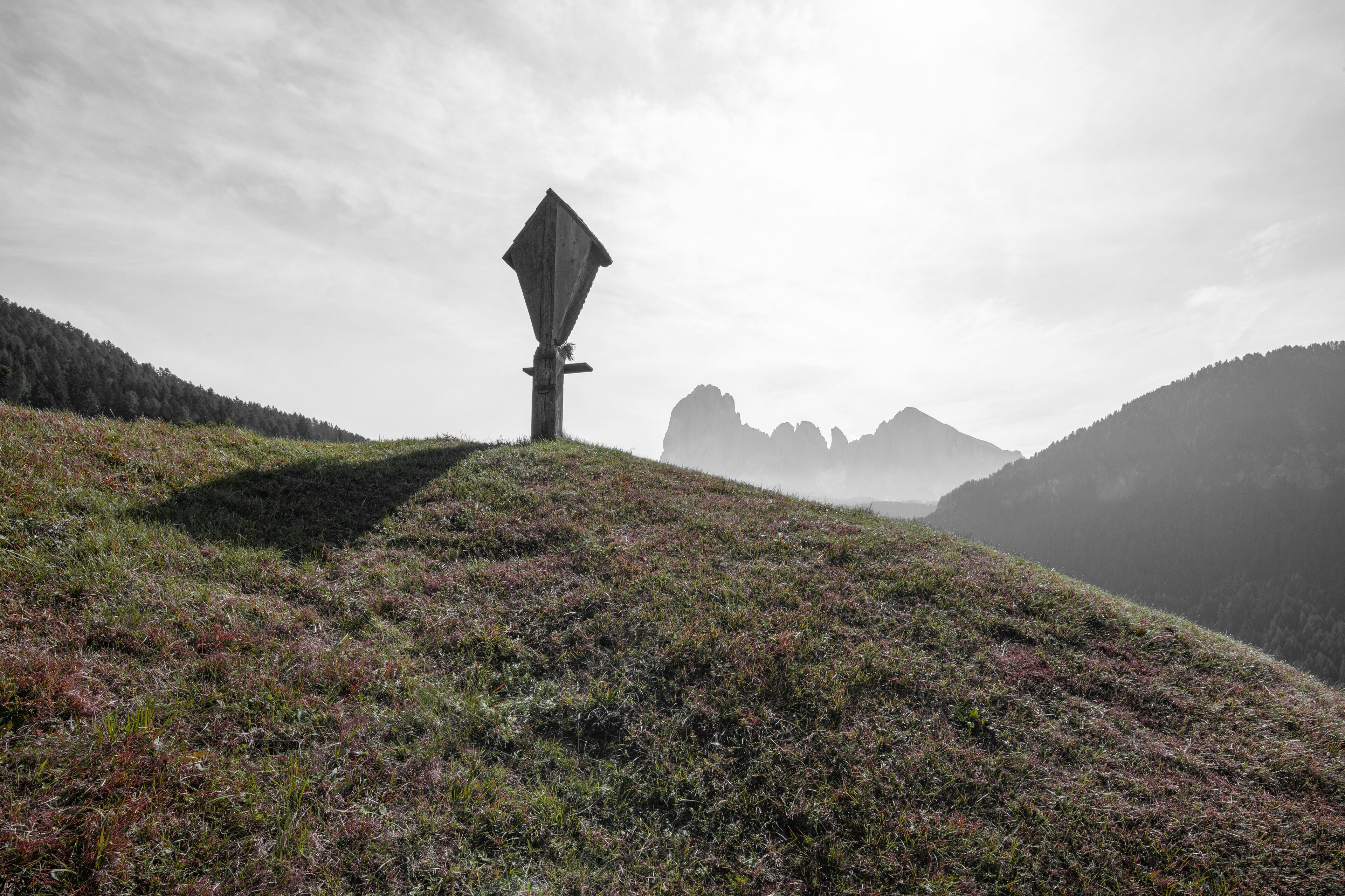 A solitary windmill on a grassy hill with a mountainous backdrop.