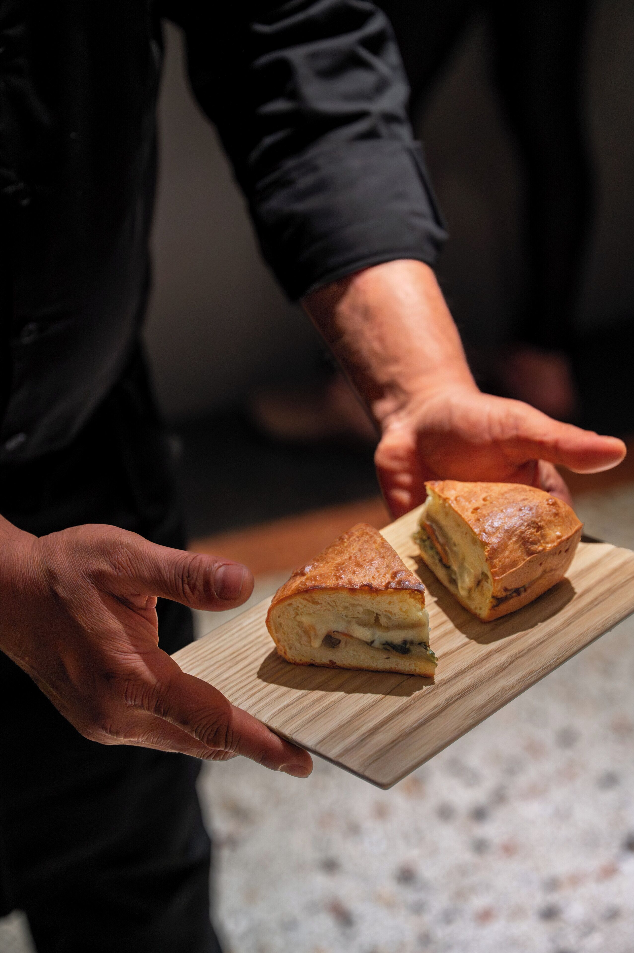 A person holding a wooden board with two sandwiches.