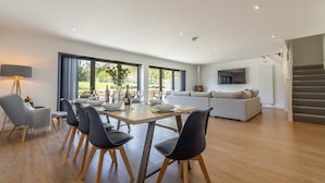 A modern living room with a dining area, a sofa, a TV, and a staircase.