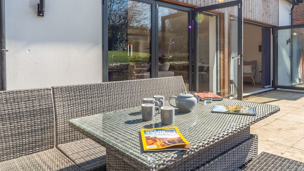 An outdoor seating area with wicker furniture, a table with a magazine, and a door leading to a covered patio.