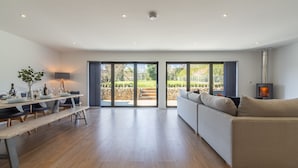 A spacious living area with a wooden floor, a sofa, a dining table with chairs, and a fireplace.