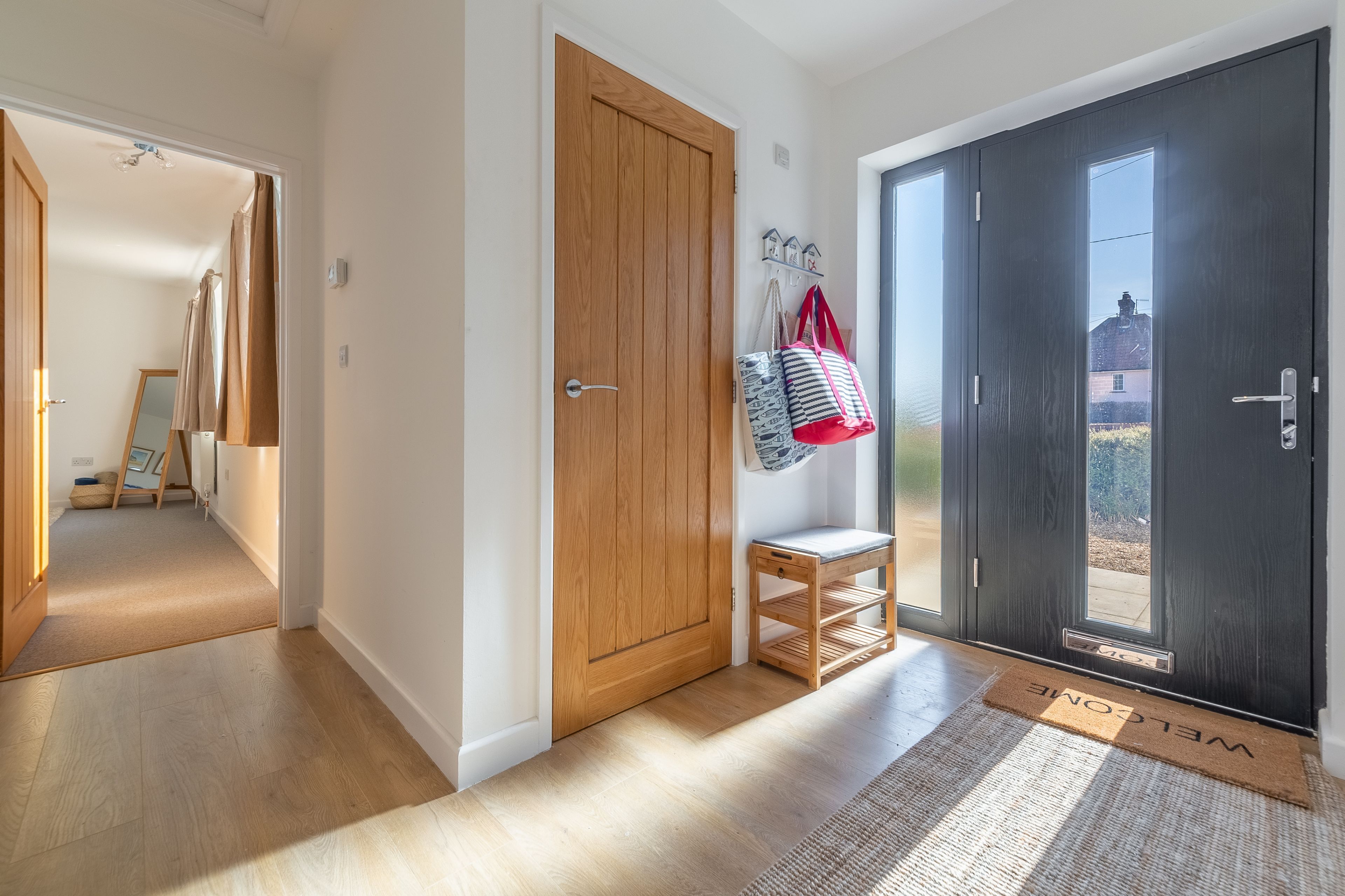 Un couloir avec une porte en bois, un banc et un paillasson.