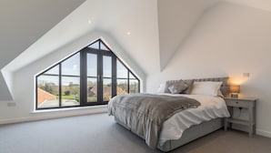 A bedroom with a large skylight, a bed with a grey and white duvet, and a bedside table with a lamp.