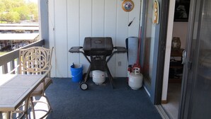 Ein Balkon mit Grill, einem blauen Eimer und einer Gasflasche.